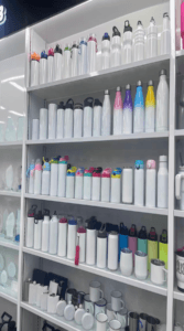 Shelves filled with various white sublimation blanks, including stainless steel sports bottles, gradient water bottles, and ceramic coffee mugs for heat transfer printing.