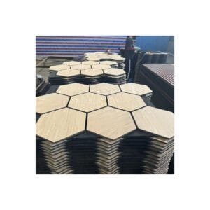 Stacks of hexagon-shaped wood slat acoustic wall panels with light oak finish and black felt backing in a factory setting.